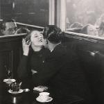 black and white photo of a couple kissing at a cafe table